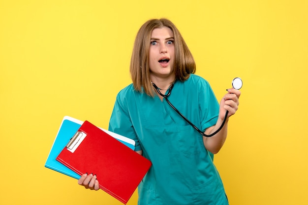 Front view of female doctor with tonometer and files on a yellow wall