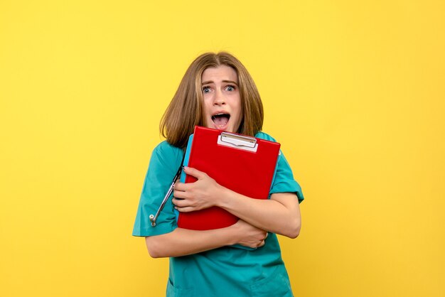 Front view of female doctor with tonometer and files on yellow wall