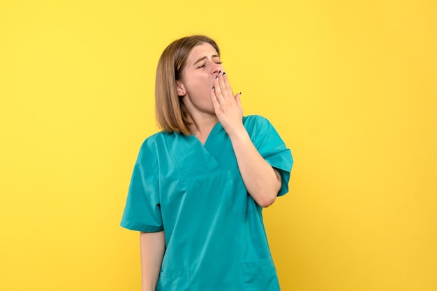 Front view of female doctor yawning on yellow wall
