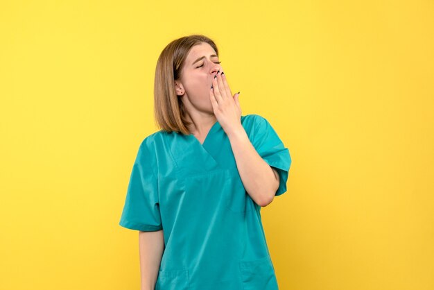 Front view of female doctor yawning on yellow wall