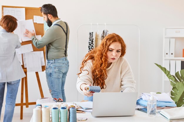 Front view of female fashion designer working in atelier with colleagues and laptop