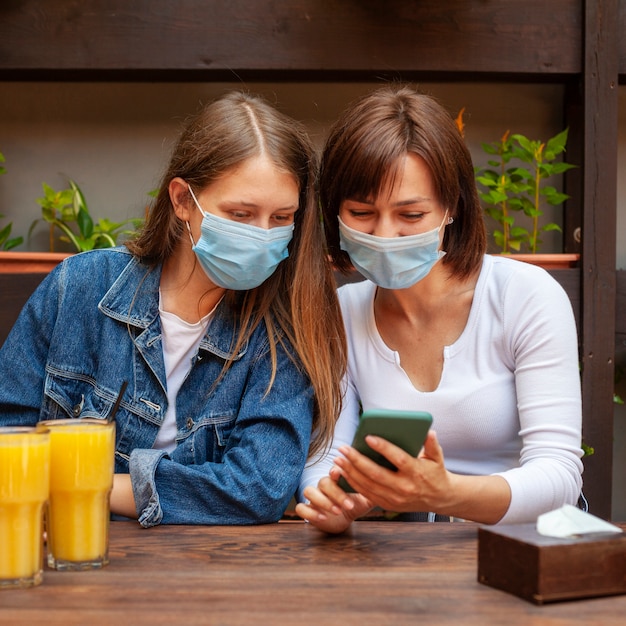 Free photo front view of female friends looking at smartphone while having some juice