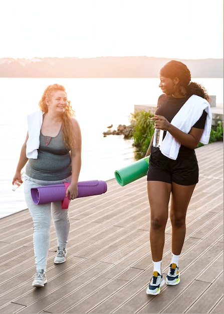 Front view of female friends walking by the lake with yoga mats