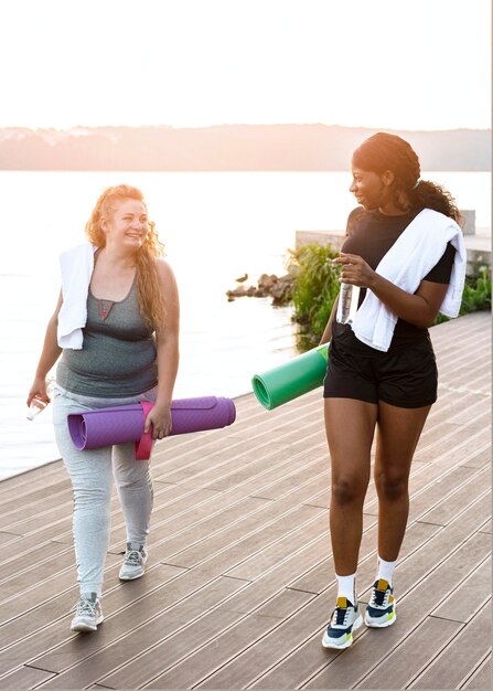 Front view of female friends walking by the lake with yoga mats