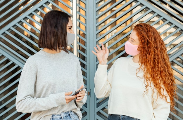 屋外で会話するフェイスマスクを持つ女性の友人の正面図