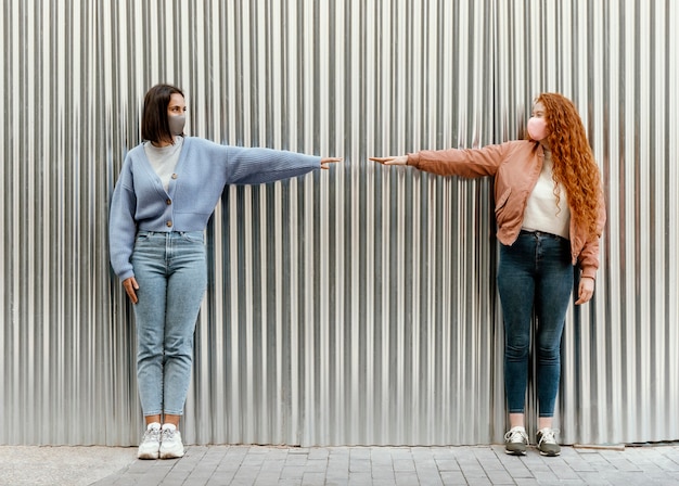 Front view of female friends with face masks outdoors touching fingers