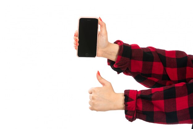 A front view female hand in black-red checkered shirt holding smartphone on the white