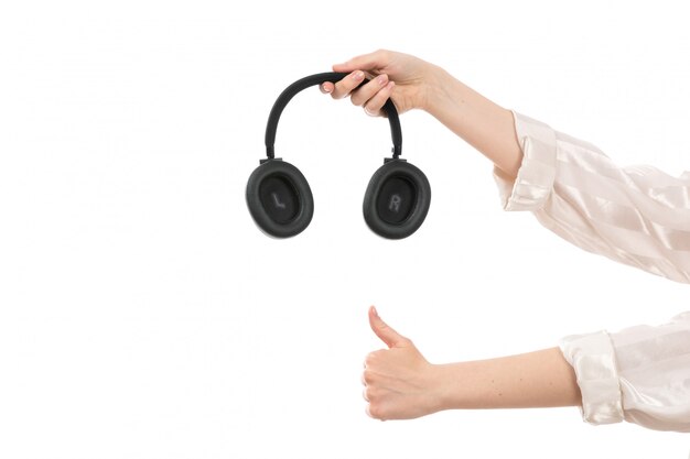 A front view female hand holding black earphones on the white