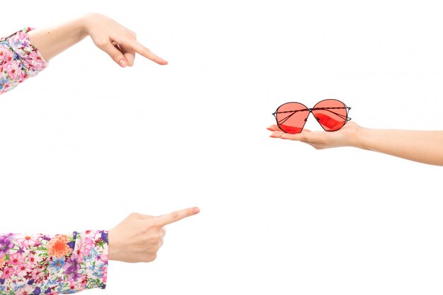 A front view female hand holding red sunglasses with other female pointing out into the sunglasses on the white