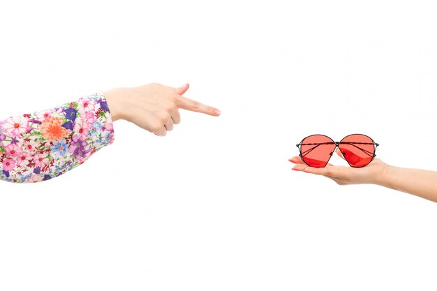 A front view female hand holding red sunglasses with other female pointing out into the sunglasses on the white
