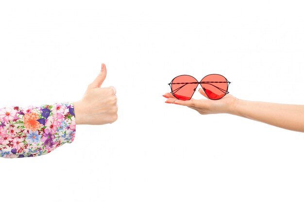 A front view female hand holding red sunglasses with other female showing awesome sign on the white