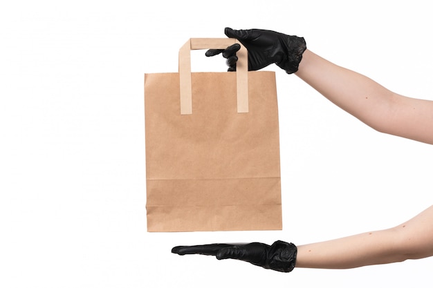 A front view female hand wearing black gloves holding paper package on white