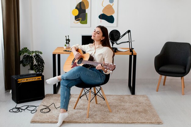 Front view of female musician playing acoustic guitar at home