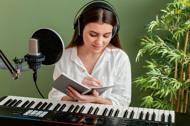 Front view of female musician playing piano keyboard and writing songs while recording