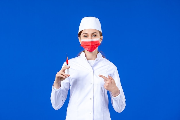 Free photo front view female nurse in white medical suit with red mask and injection in her hands on blue