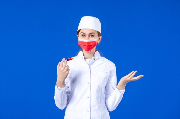 파란색에 그녀의 손에 빨간 마스크와 주사 흰색 의료 소송에서 전면보기 여성 간호사