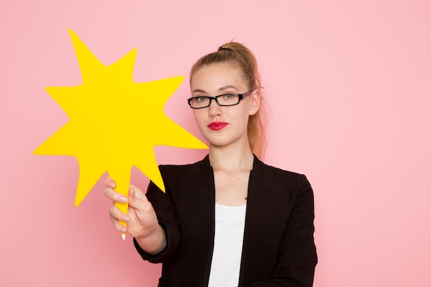 Foto gratuita vista frontale dell'impiegato femminile in giacca rigorosa nera che tiene un enorme cartello giallo sulla parete rosa