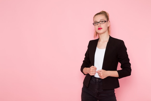 Front view of female office worker in black strict jacket just posing on the pink wall