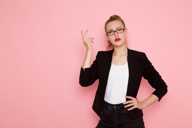 Front view of female office worker in black strict jacket posing on the pink wall