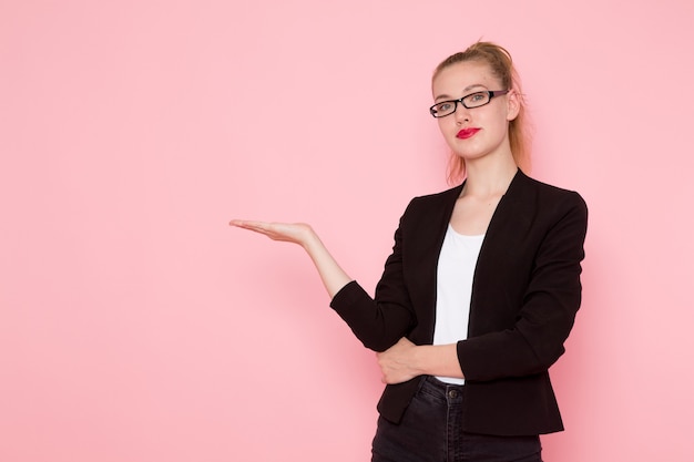 Free photo front view of female office worker in black strict jacket raising her hand on light-pink wall