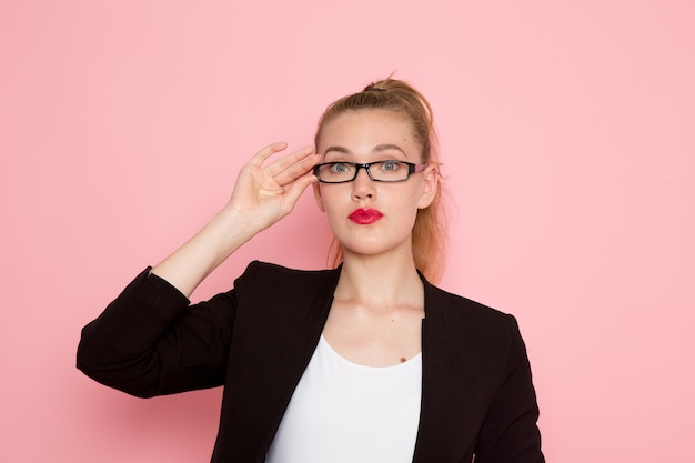 Front view of female office worker in black strict jacket wearing optical sunglasses on pink wall