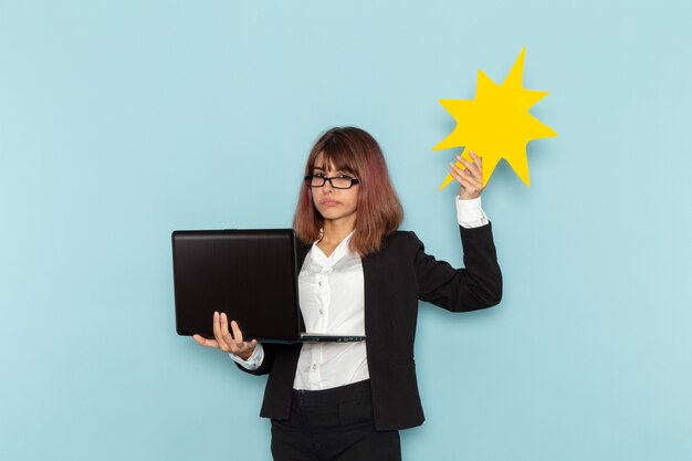 Front view female office worker holding huge yellow sign and laptop on the blue surface