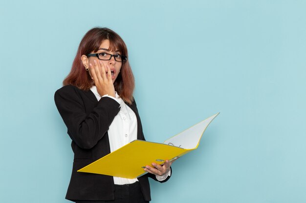 Front view female office worker holding and reading document on the blue surface