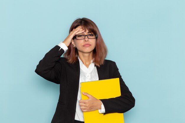 Front view female office worker holding yellow documents on blue surface