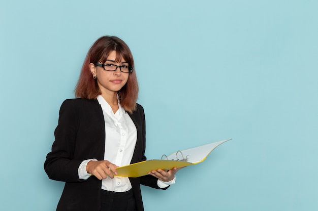 Front view female office worker holding yellow documents on the light-blue surface