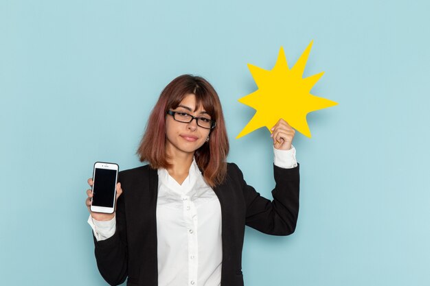 Front view female office worker in strict suit holding yellow sign with phone on blue surface