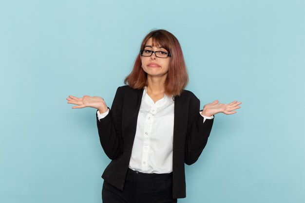 Front view female office worker in strict suit posing on the blue surface