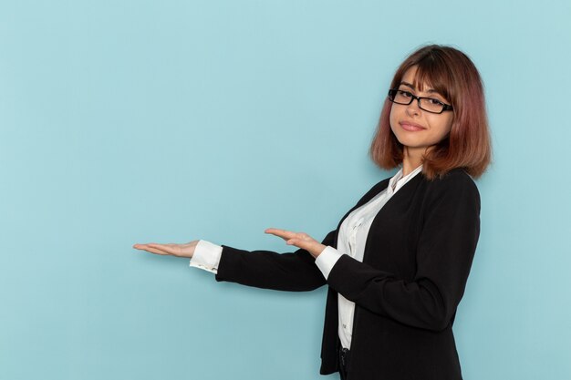 Front view female office worker in strict suit posing on light-blue desk