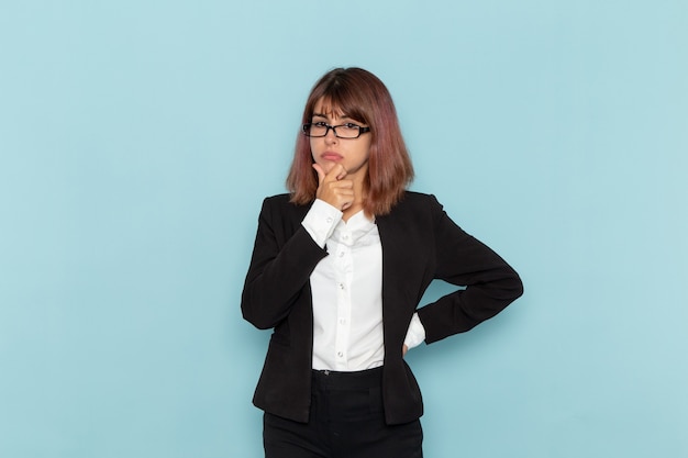 Front view female office worker in strict suit posing and thinking on blue surface