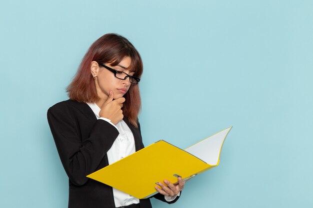 Front view female office worker in strict suit reading document on blue surface