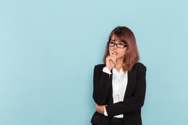 Front view female office worker in strict suit thinking on blue surface