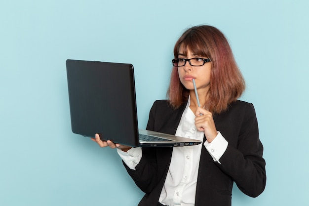 Front view female office worker in strict suit using laptop on light blue surface