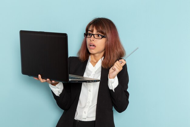 Front view female office worker in strict suit using laptop on the light-blue surface