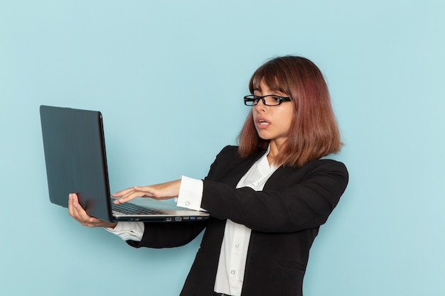 Front view female office worker in strict suit using laptop on the light blue surface