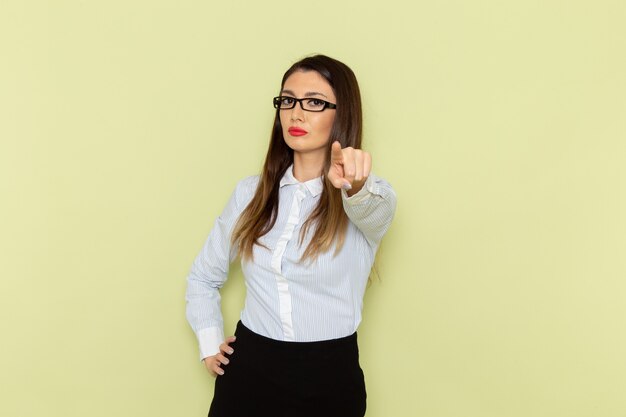 Front view of female office worker in white shirt and black skirt on green wall