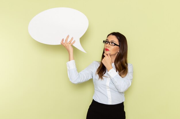 Front view of female office worker in white shirt and black skirt holding big white sign on light-green wall