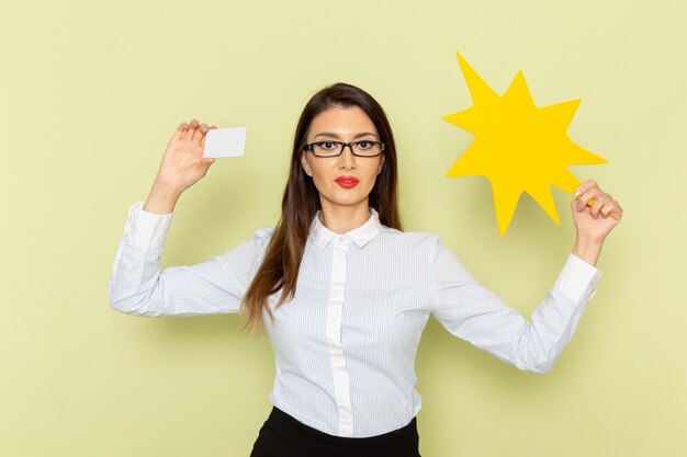 Front view of female office worker in white shirt and black skirt holding big yellow sign on green wall