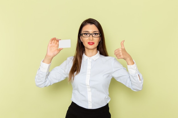 Vista frontale dell'impiegato femminile in camicia bianca e gonna nera che tiene la carta di plastica sulla parete verde chiaro