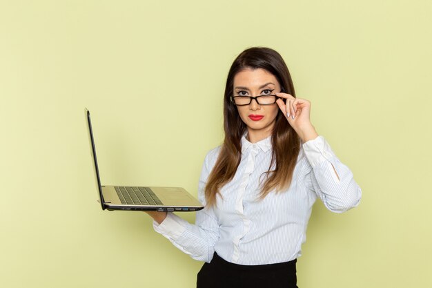 Front view of female office worker in white shirt and black skirt holding using laptop on green wall