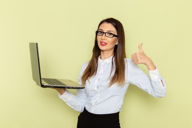 Front view of female office worker in white shirt and black skirt holding using laptop on green wall