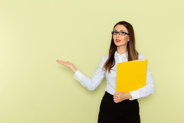 Front view of female office worker in white shirt and black skirt holding yellow file on green wall