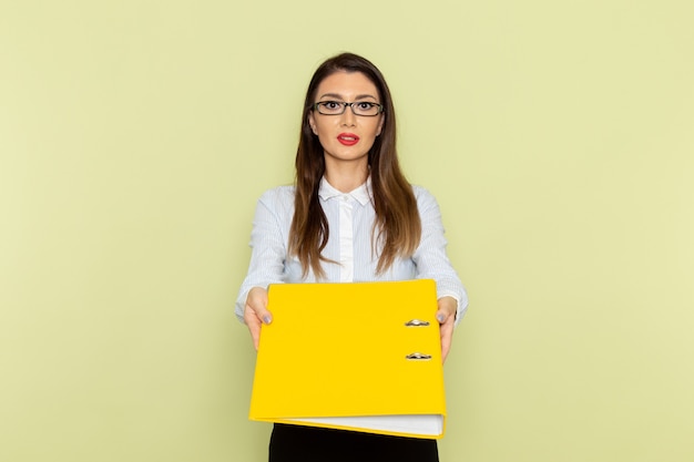 Free photo front view of female office worker in white shirt and black skirt holding yellow file on green wall