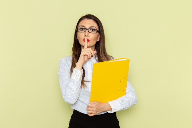 Front view of female office worker in white shirt and black skirt holding yellow file on the green wall