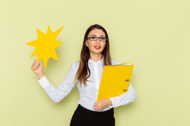 Front view of female office worker in white shirt and black skirt holding yellow file and sign on green wall