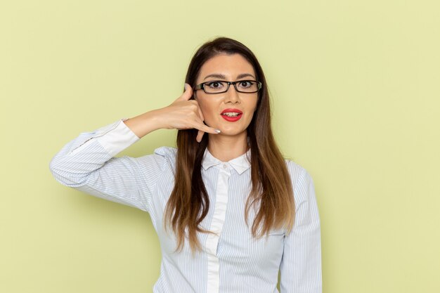 Front view of female office worker in white shirt and black skirt posing on light-green wall