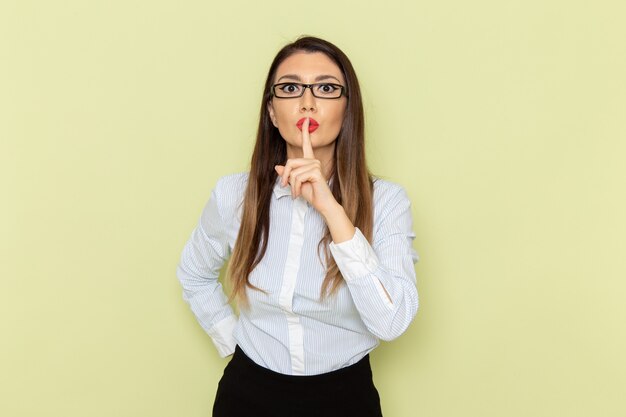 Front view of female office worker in white shirt and black skirt showing silence sign on green wall